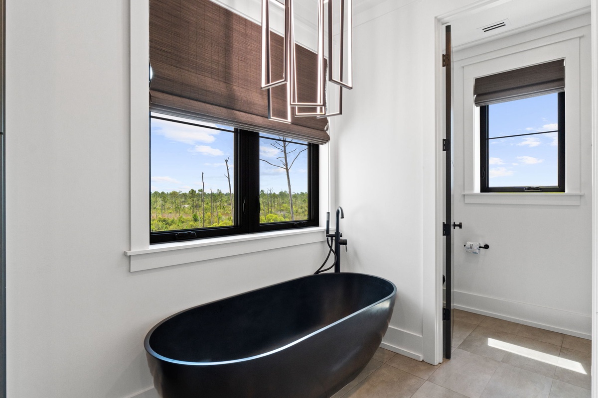 Soak away your cares in this striking black freestanding tub. Natural light pours in through windows framing peaceful treetop views, while elegant pendant lights add a sophisticated glow.
