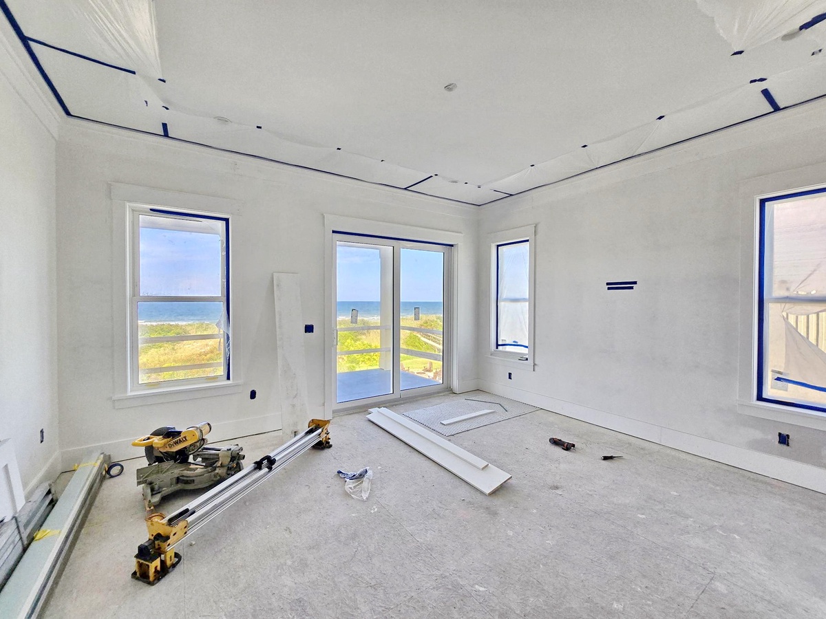 A bright, spacious room under construction with stunning ocean views through multiple windows—soon you'll enjoy coastal breezes and natural light filling your home.