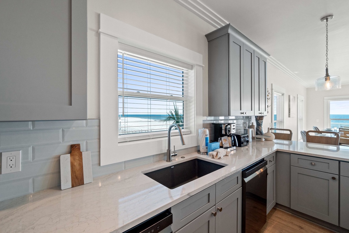 Your coastal kitchen features modern gray cabinets, quartz countertops, and stunning ocean views through bright windows—perfect for morning coffee or preparing meals.