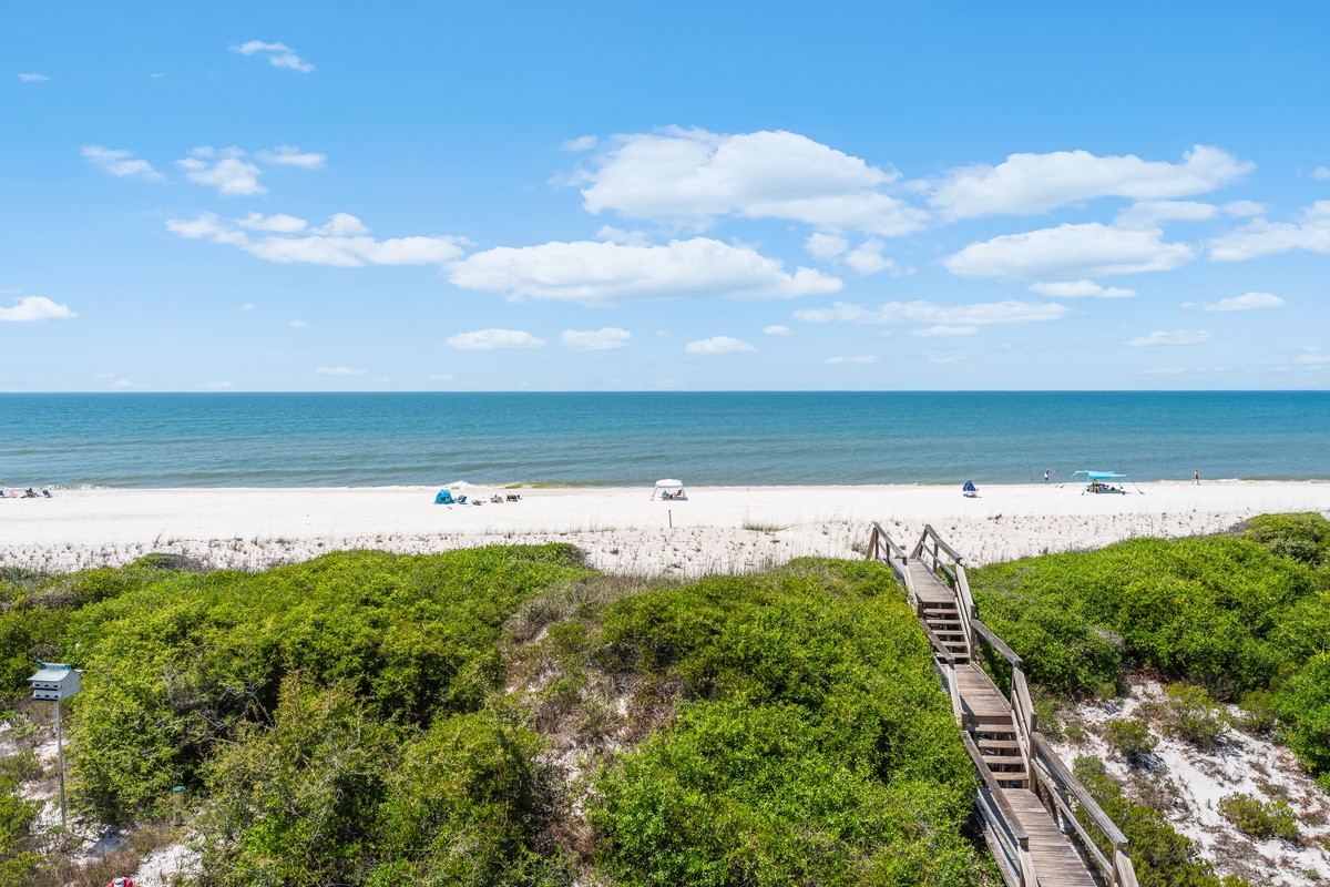 Pristine white sand beach stretches along turquoise waters, with wooden boardwalk providing easy access through coastal dunes.