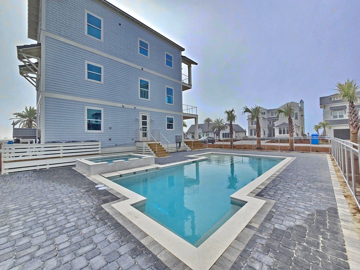 Modern coastal property featuring a pristine swimming pool with hot tub and elegant paver deck.