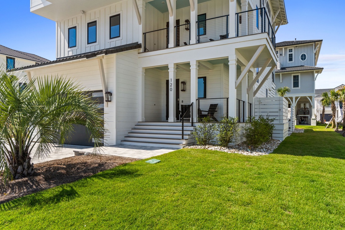 A beautifully designed coastal retreat with modern architecture, welcoming front porch, and lush tropical landscaping featuring palm trees and manicured lawn in a peaceful neighborhood setting.