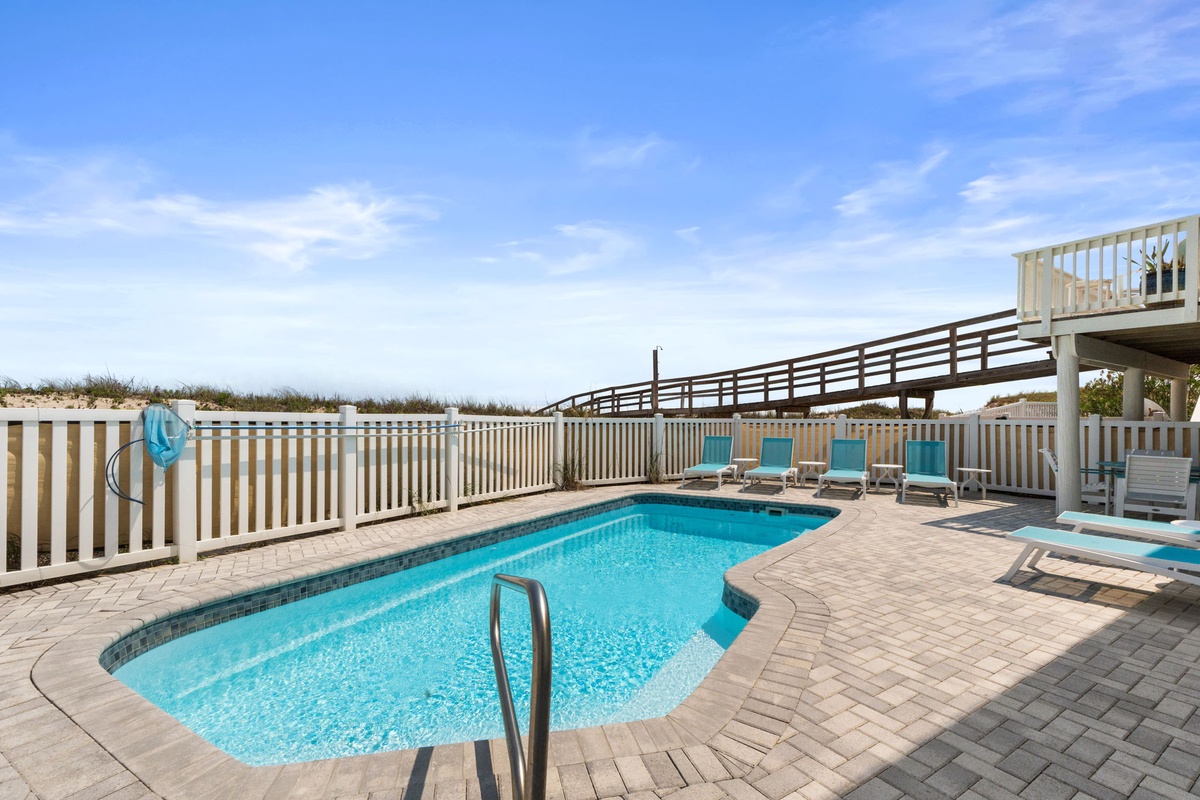 A sparkling pool awaits with turquoise loungers perfectly positioned for sunbathing, all set against a backdrop of natural dunes and open sky.