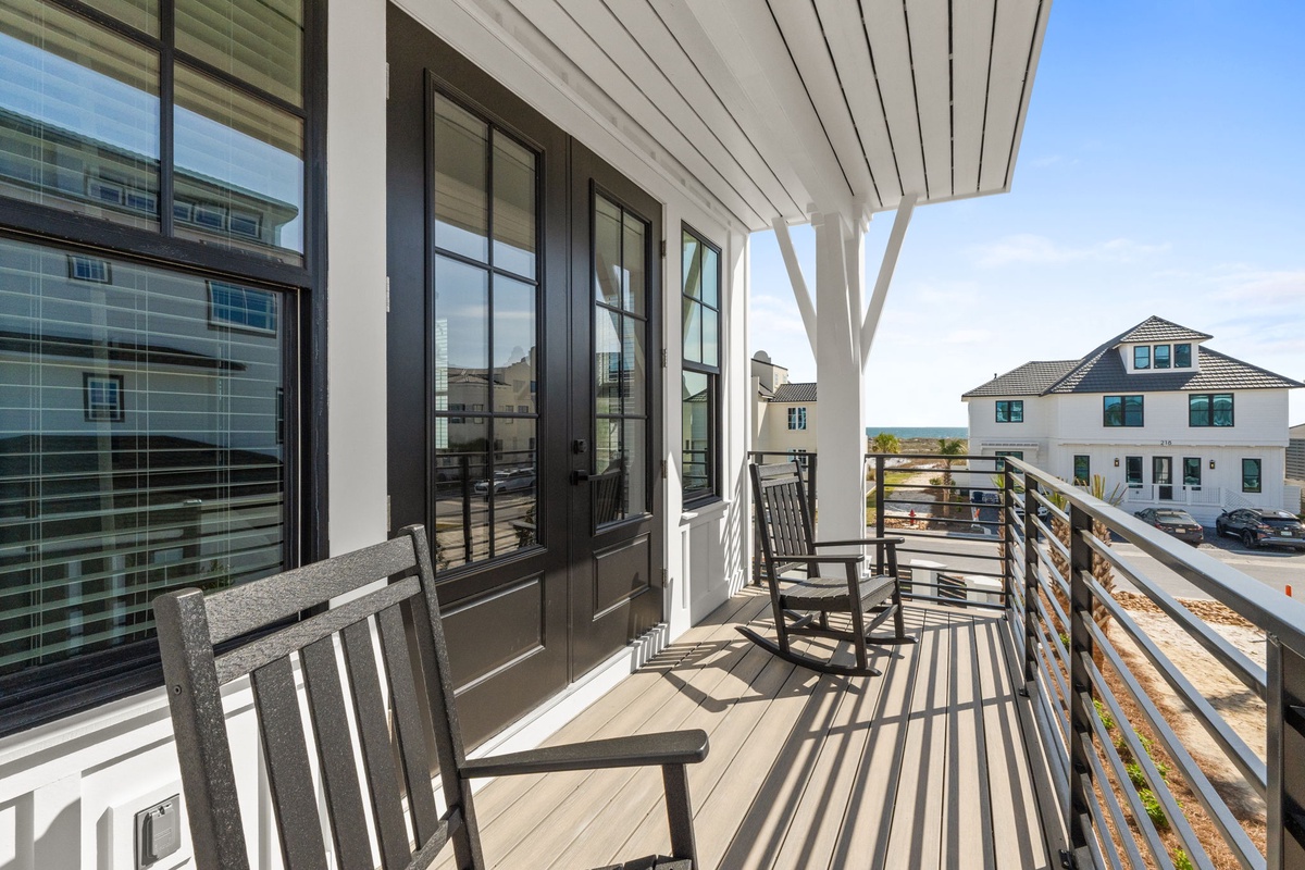 Modern balcony with comfortable seating overlooking a peaceful residential neighborhood during a bright, sunny day.