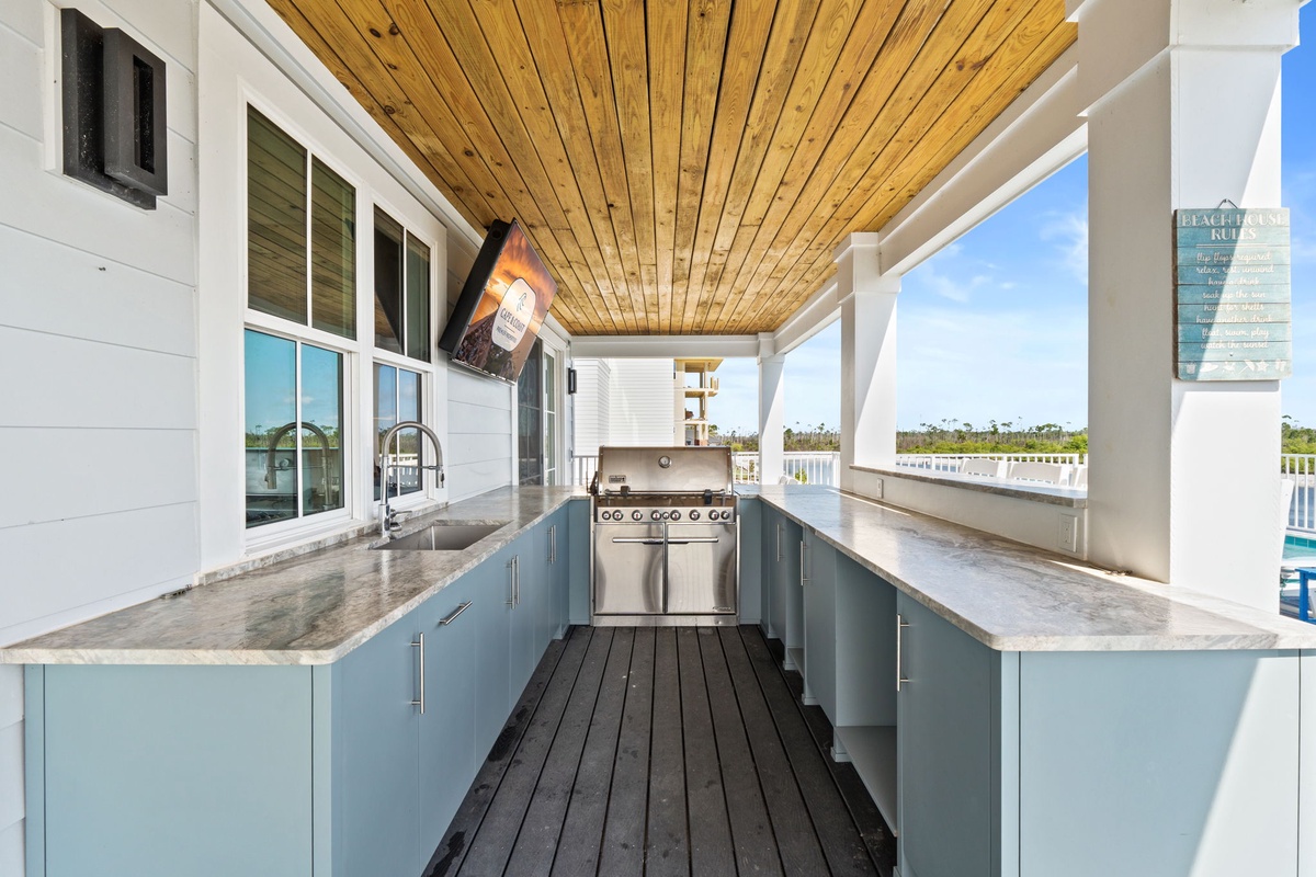 An outdoor kitchen with sleek blue cabinetry and stainless-steel grill creates the perfect setup for entertaining guests while enjoying scenic water views.