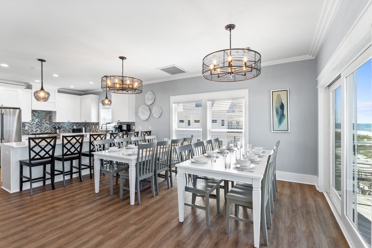 Step into an elegant open space where sparkling chandeliers illuminate your gatherings. The dining area seats everyone comfortably, while coastal views peek through expansive windows, inviting ocean breezes into your vacation home.