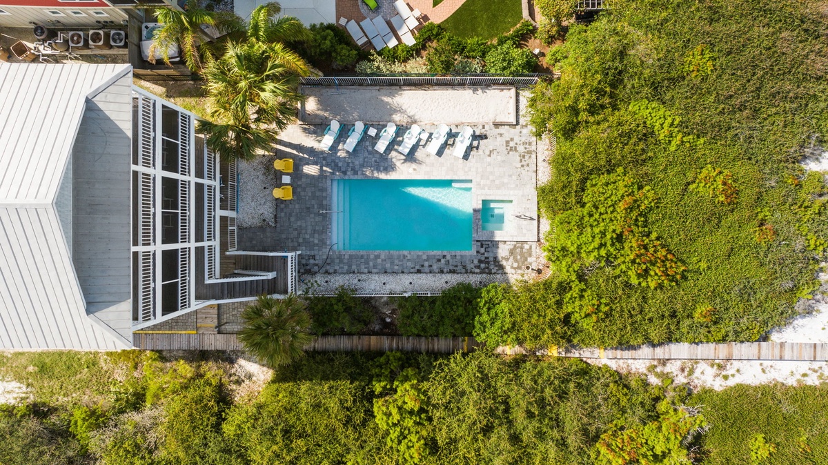 An aerial view of the property showcasing the inviting swimming pool surrounded by lounge chairs and lush tropical vegetation.