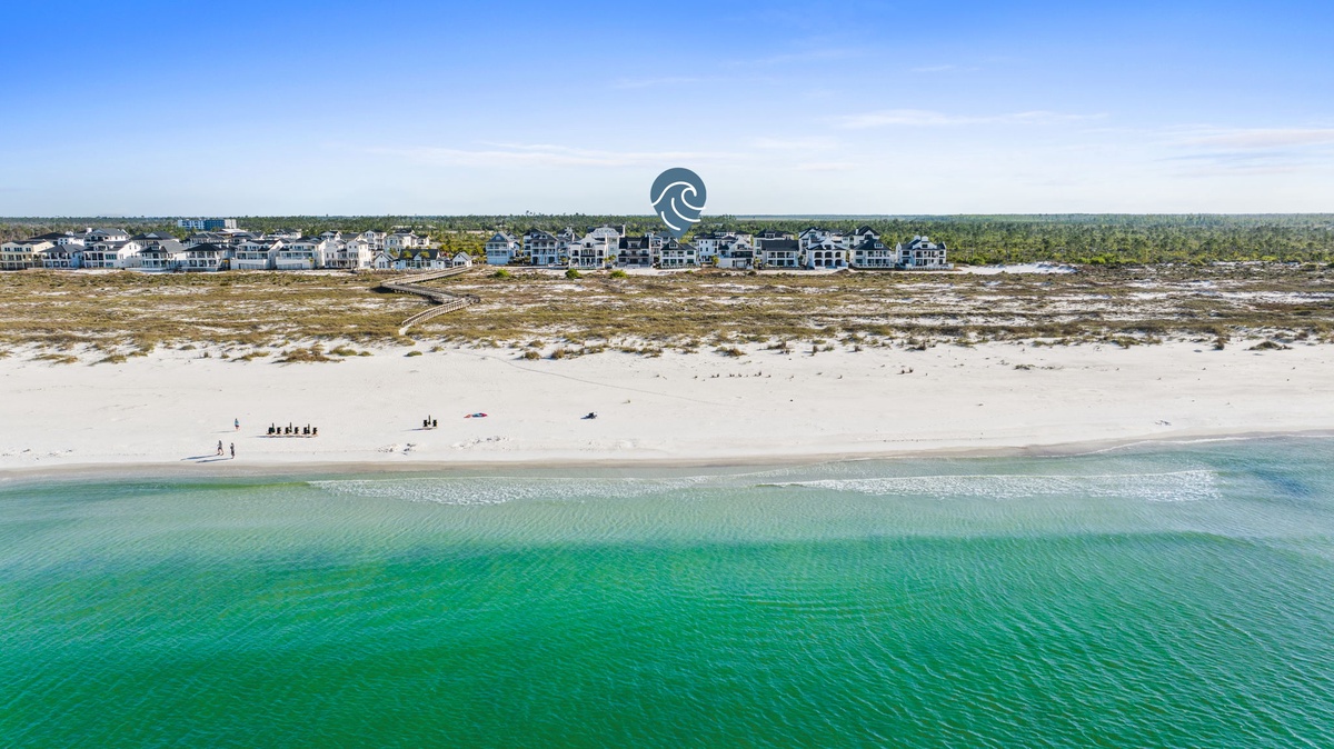 Stunning aerial view showcases pristine white sand beach meeting emerald waters, with coastal vacation homes nestled among natural dunes.
