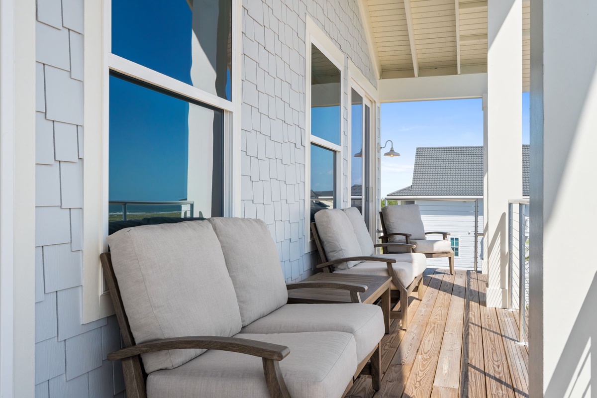 Settle into plush outdoor seating on your private balcony, where warm wood tones and coastal breezes create the perfect spot to unwind and soak in peaceful neighborhood views.