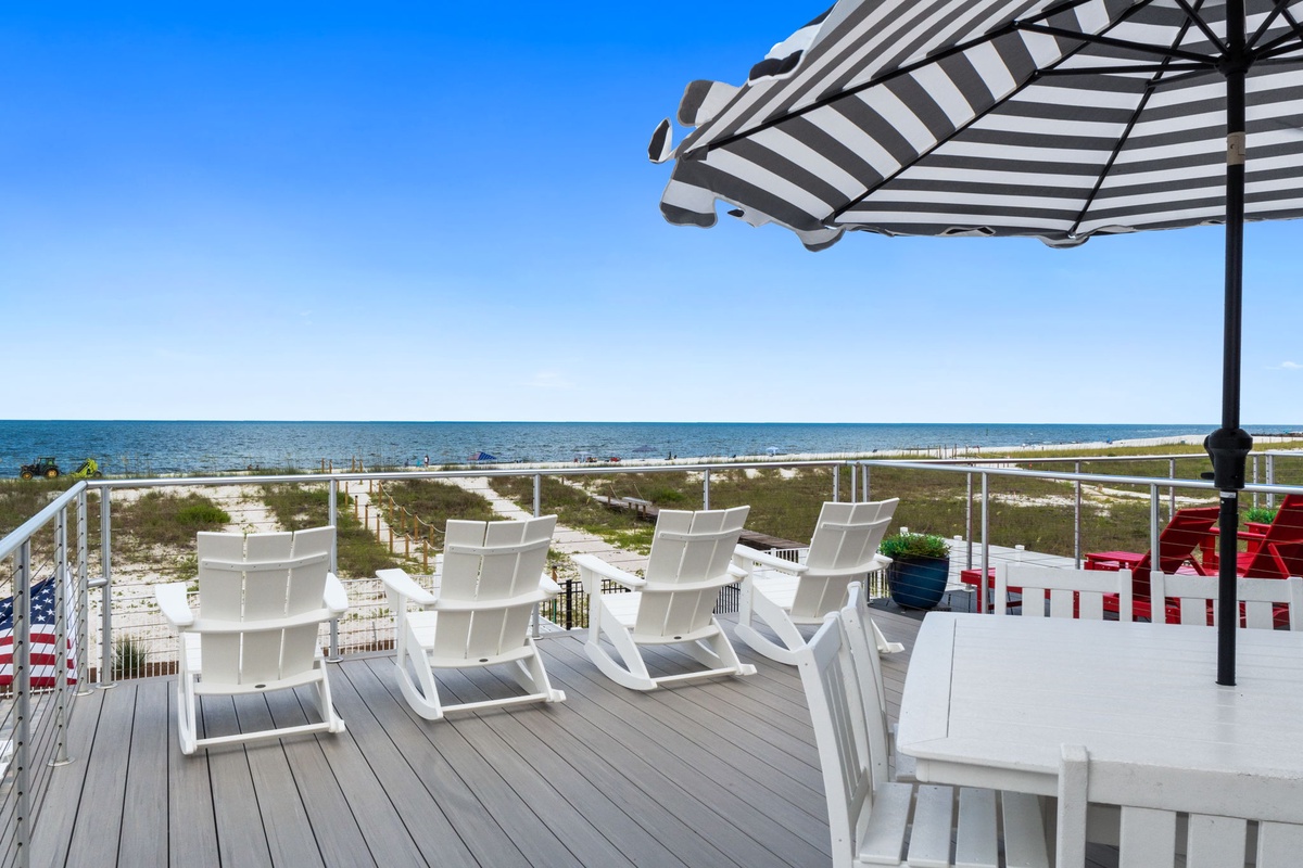 A private beachfront deck overlooks pristine shores and sparkling waters, where loungers and shaded dining await your sunny getaways.