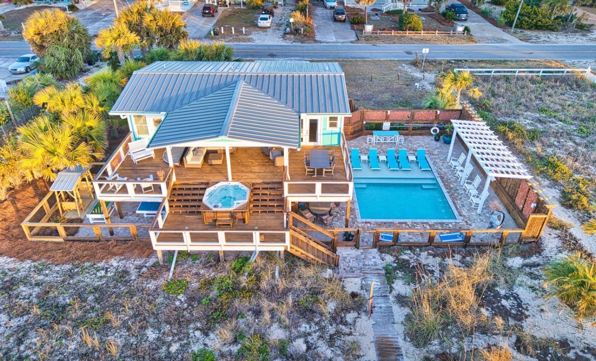 Aerial view of beachfront vacation rental featuring swimming pool, hot tub, and multi-level deck surrounded by tropical palms.