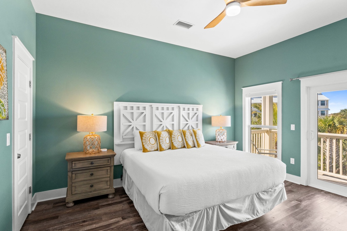 Sink into crisp white linens beneath soothing teal walls, where golden accents and gentle ceiling fan breezes create your perfect coastal retreat.