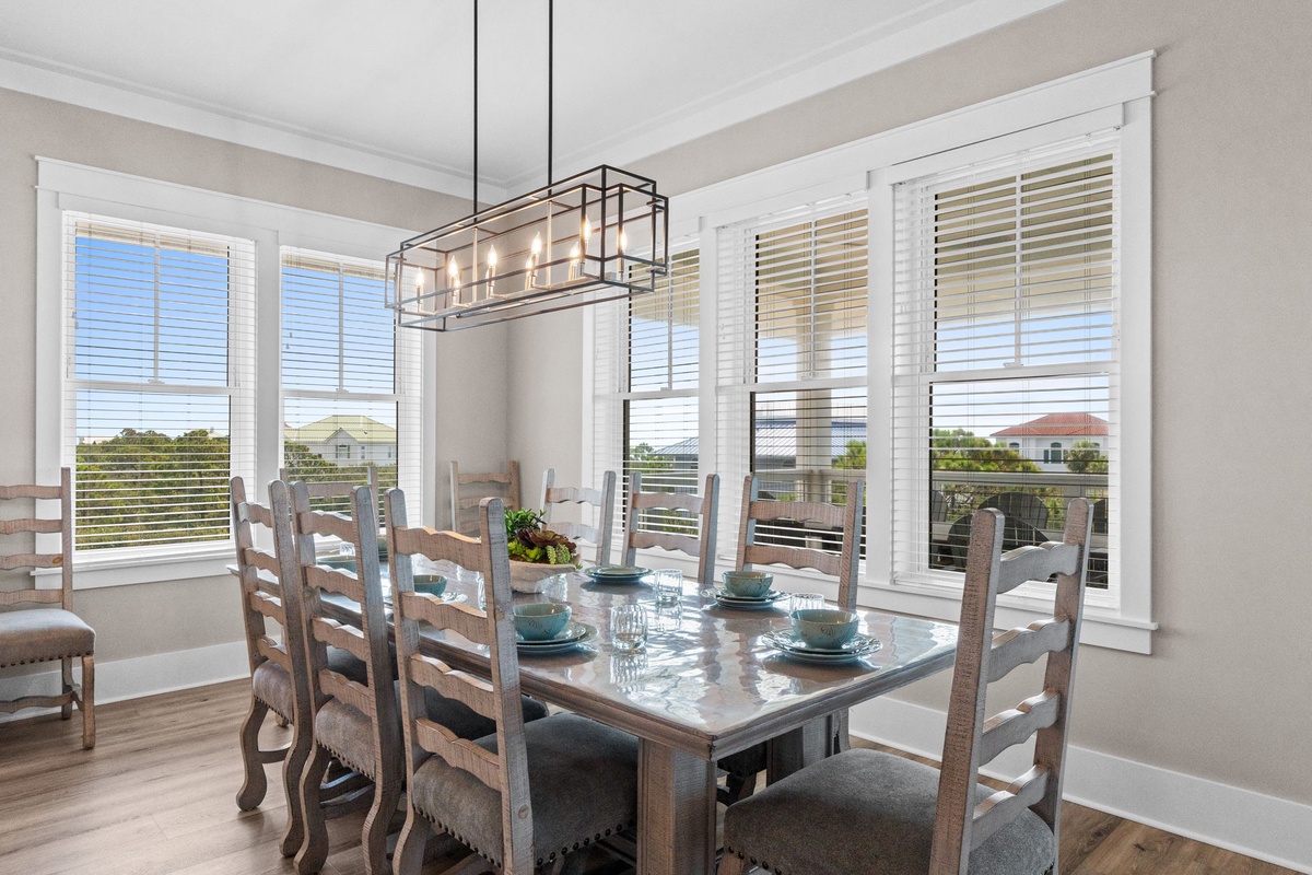 Gather around this inviting dining table, where sunlight streams through plantation shutters and the modern chandelier sets the perfect mood for your meals together.