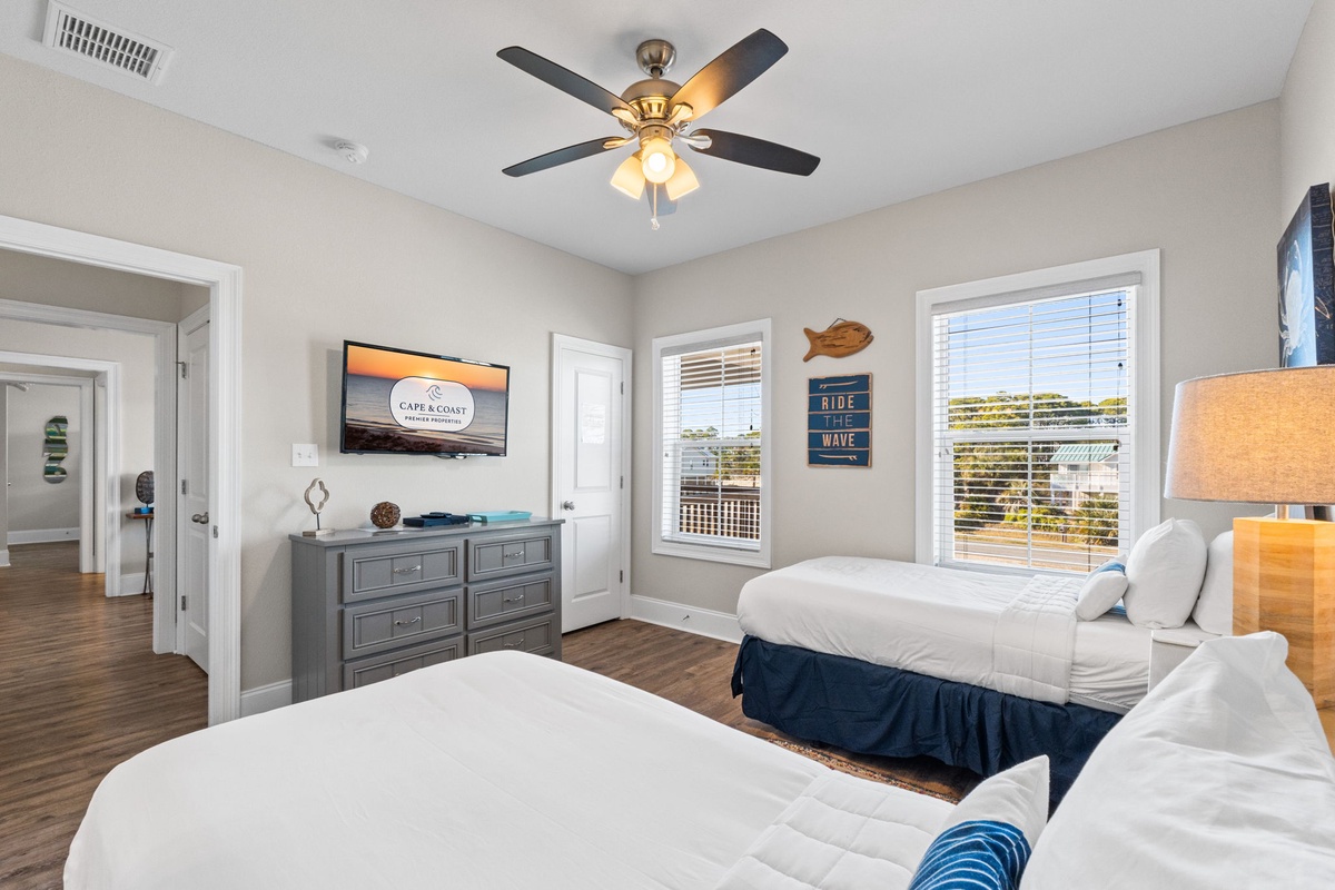 Unwind in your bright bedroom with two comfortable beds, ceiling fan, and windows overlooking the area.