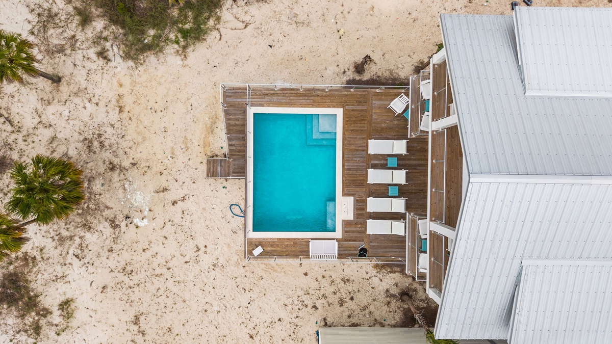 Aerial view of the property showcasing a private pool surrounded by wooden decking and sandy beachfront surroundings.