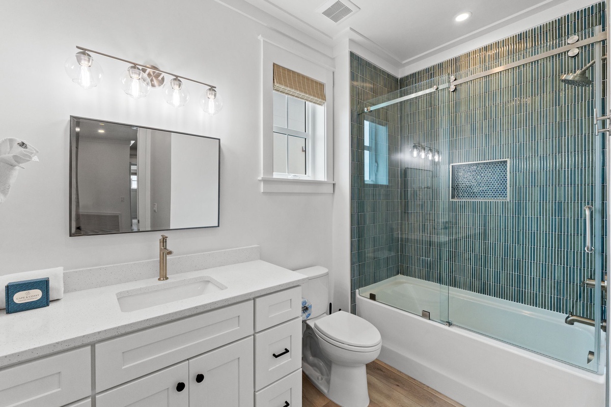 Your private bathroom features stylish vertical tile work in calming teal tones, a soaking tub with a glass enclosure, and a bright vanity with soft overhead lighting for your daily routine.