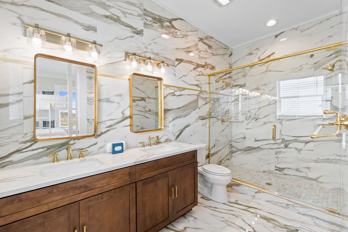 Step into luxury with marble walls, gold fixtures, and a spacious glass shower in this elegant bathroom retreat.