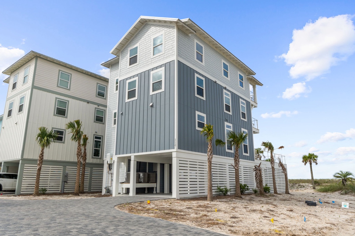 A modern three-story coastal property featuring elevated construction, palm tree landscaping, and convenient parking at the entrance, situated steps from the beach in a beautiful sunny location.