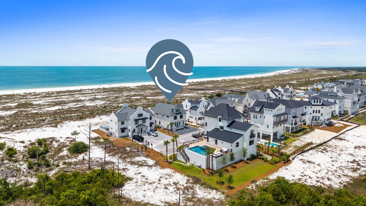 Coastal residential community featuring modern vacation homes with pristine white sandy beaches and turquoise Gulf waters nearby, offering an idyllic beachside retreat setting.