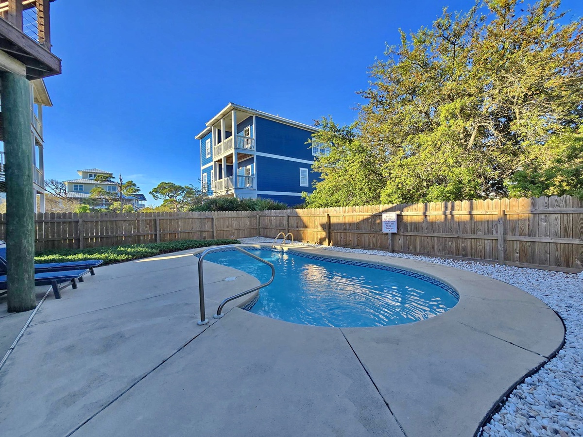 Private pool oasis with crystal-clear water surrounded by coastal charm and vibrant blue skies.