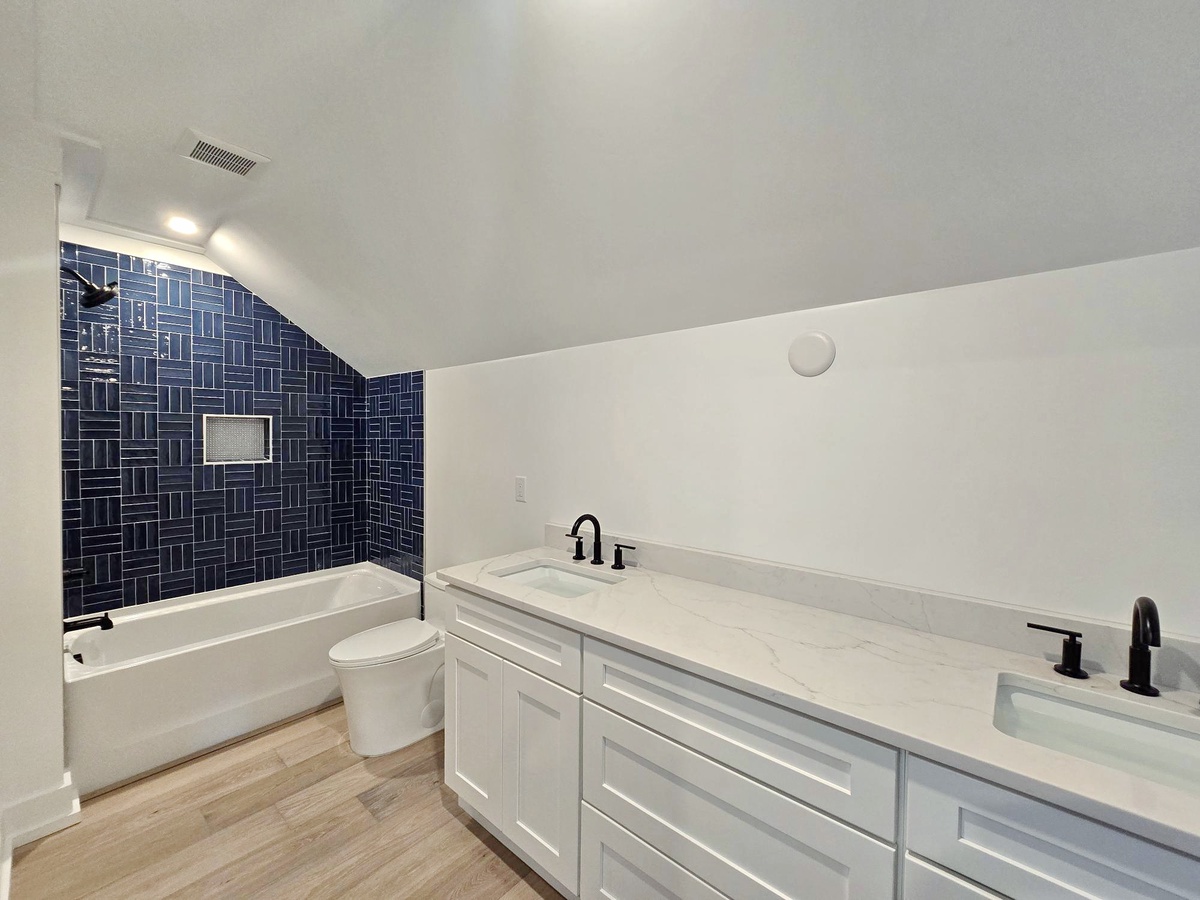 Unwind in your elegant bathroom featuring a soaking tub, dual vanity, and stunning navy herringbone tile accent wall.