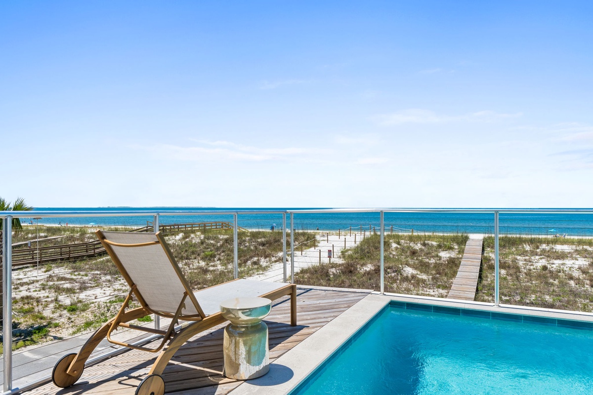 Expansive beachfront property featuring direct beach access via private boardwalk, private pool deck, and unobstructed ocean views across white sand dunes under clear coastal skies.