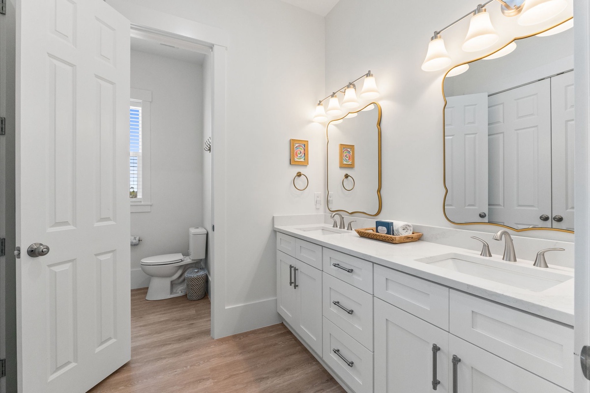 Your spacious bathroom features dual sinks with elegant gold-rimmed mirrors and warm vanity lighting, creating a luxurious morning routine.