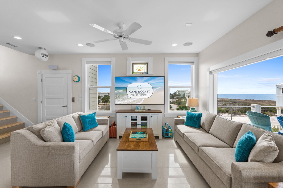 Sink into plush gray sofas with ocean views stretching endlessly beyond your windows, while ceiling fans keep you cool.