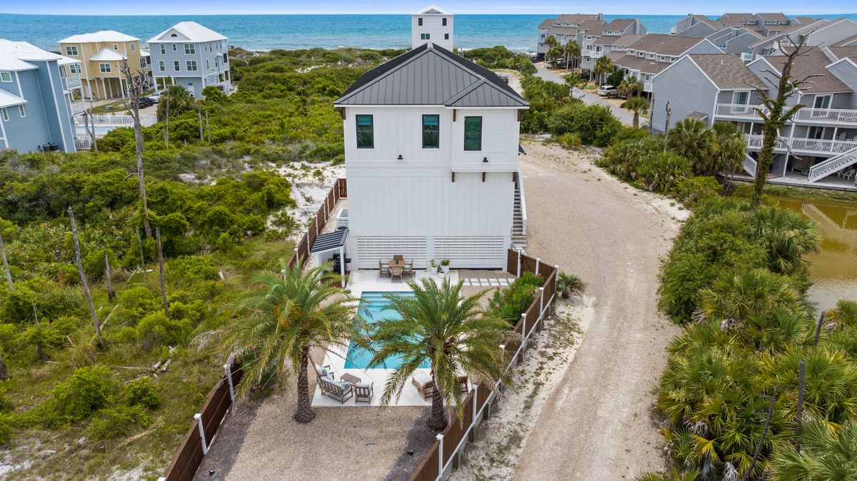Coastal vacation home featuring a private pool, tropical palms, and fenced courtyard, situated steps from the beach in a lush island neighborhood.