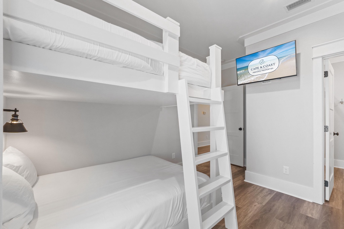 Your cozy bedroom features custom bunk beds with crisp white linens and a welcoming coastal vibe, offering comfortable sleeping arrangements for your entire group.