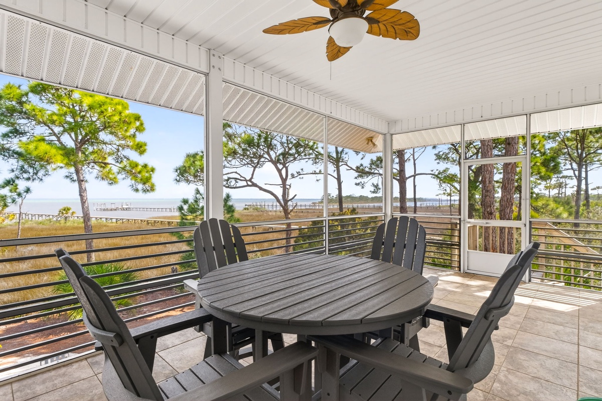 Your private screened porch offers waterfront dining with coastal breezes and stunning views through towering pines to the bay beyond.