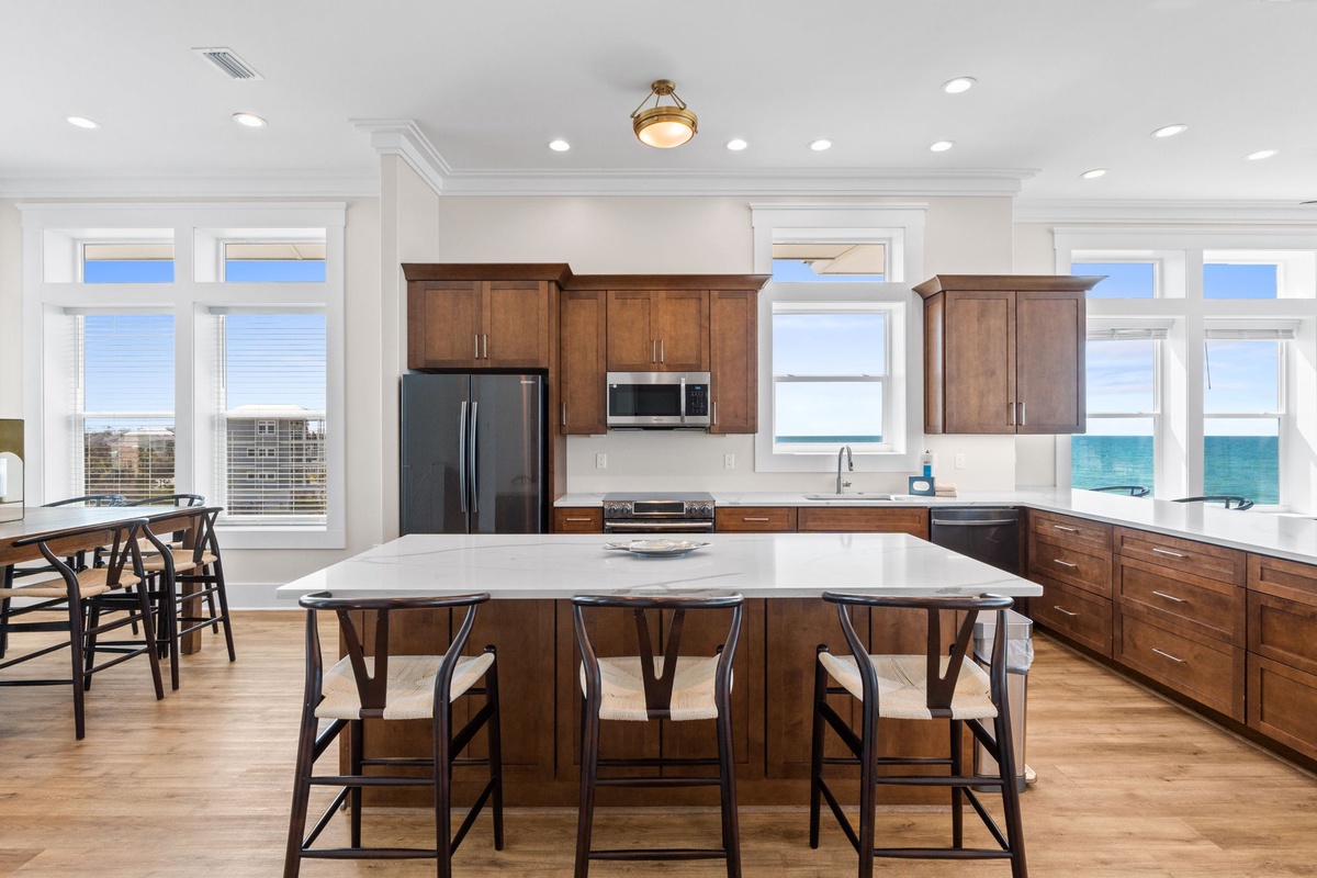 Your gourmet kitchen awaits with gleaming countertops, rich wood cabinetry, and stunning ocean views through wraparound windows.