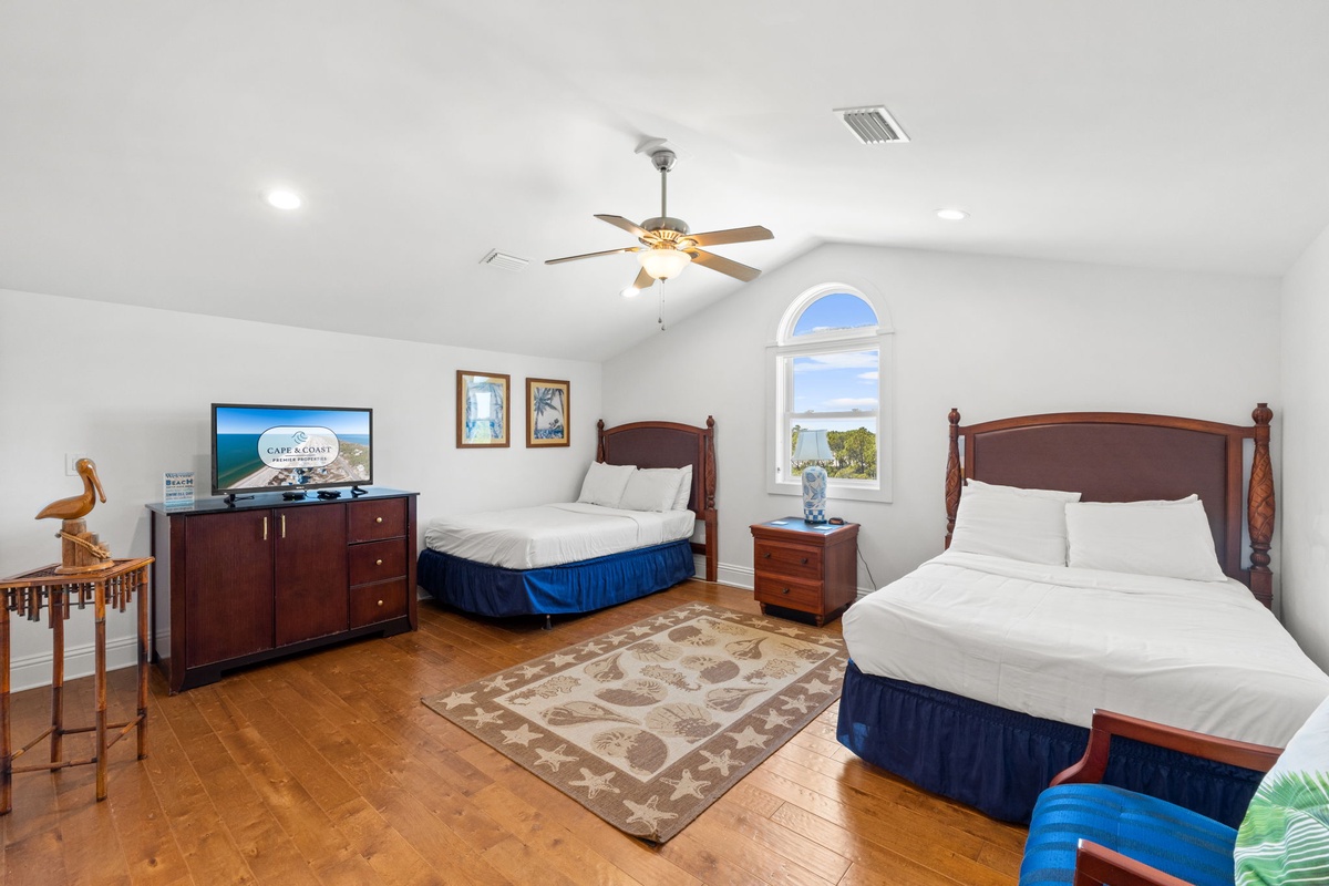 Your spacious bedroom features two plush beds with elegant wooden headboards, a ceiling fan to keep you cool, and a charming arched window offering serene water views.