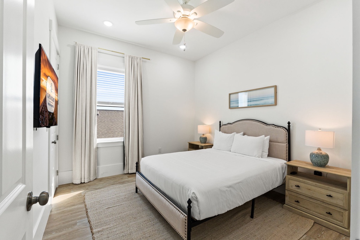 Sink into crisp white linens in your serene bedroom, where natural light filters through soft curtains and a gentle ceiling fan keeps you comfortable.