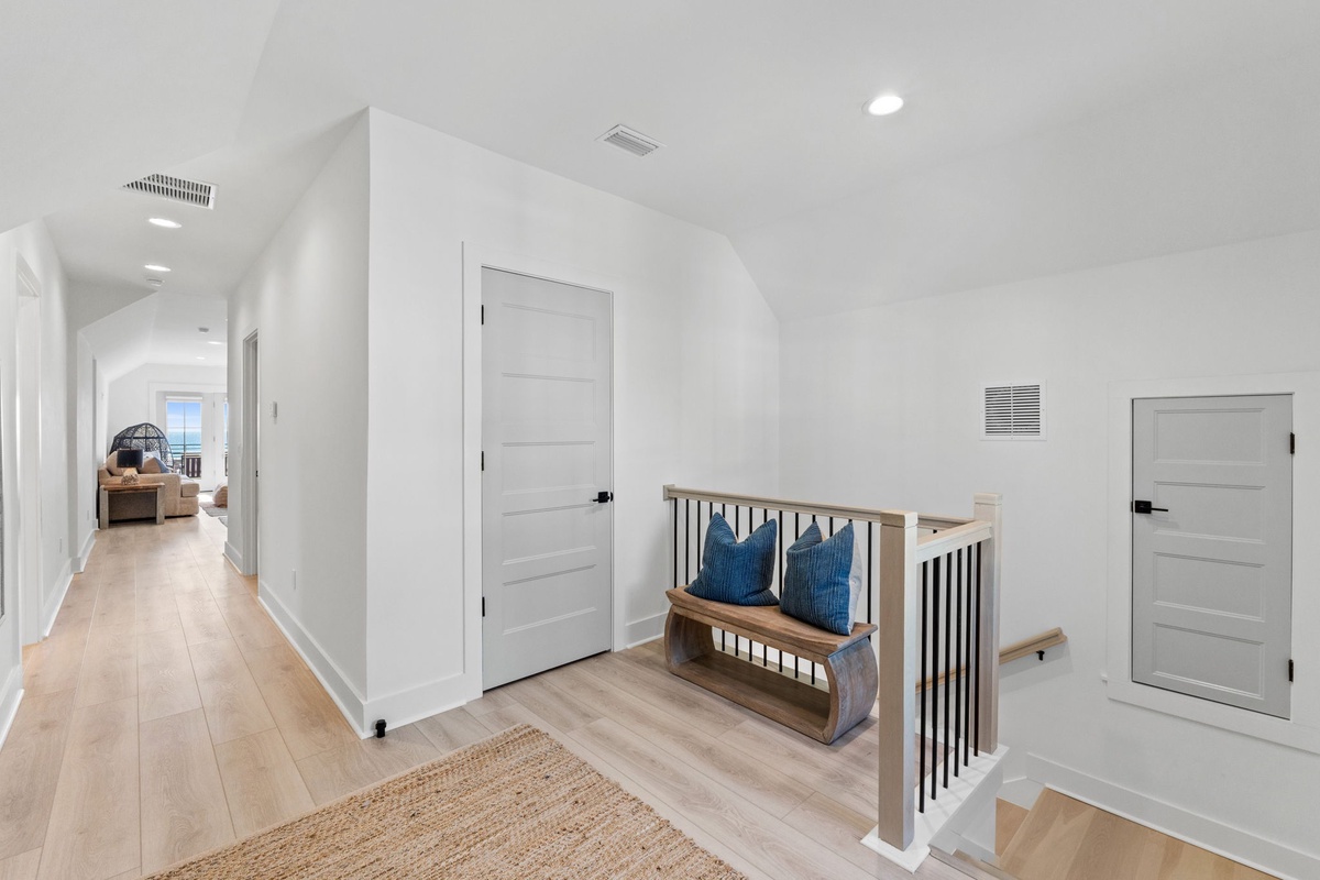 Your stylish upstairs hallway features gleaming hardwood floors and a cozy reading nook with blue pillows—perfect for quiet moments.