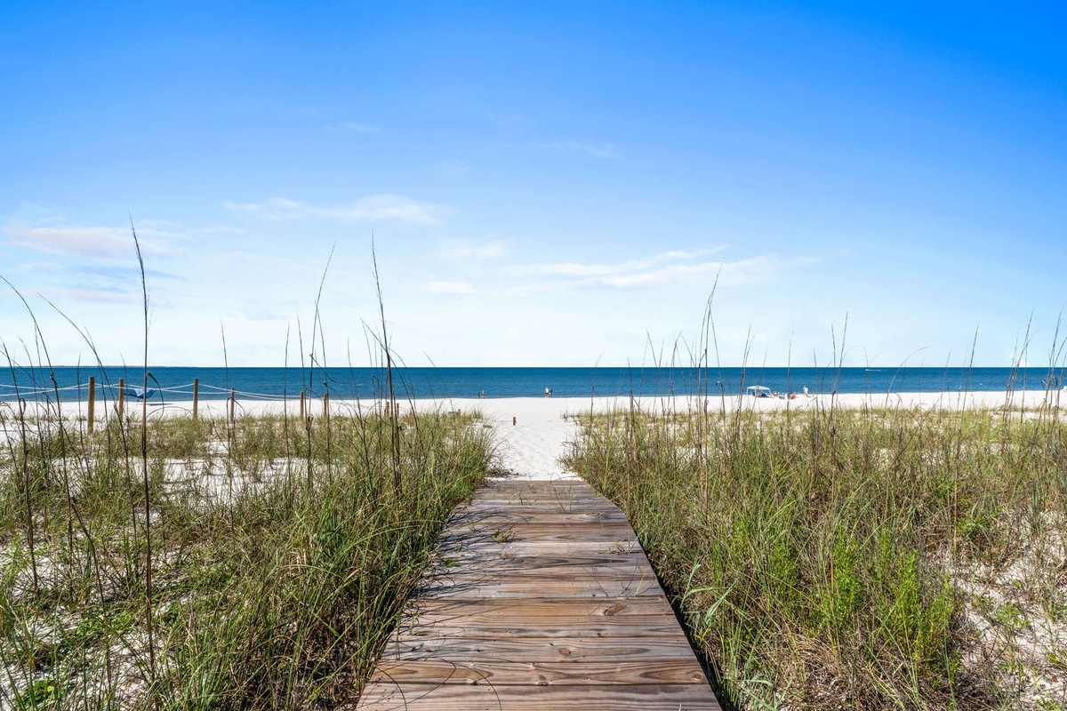 A wooden boardwalk leads through natural dunes to pristine white sands and sparkling turquoise waters—your private path to endless beach days and coastal serenity.