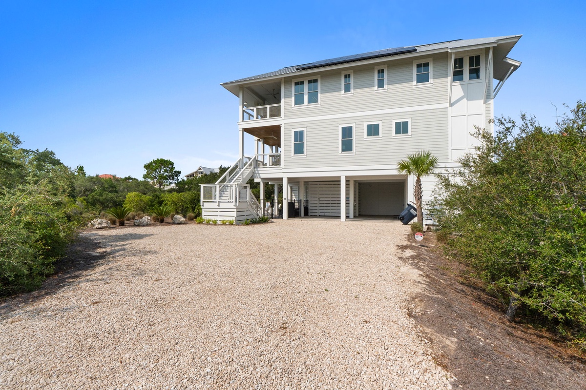 This spacious coastal home features three levels of living space with covered balconies and ground-level parking, nestled among native vegetation near the beach.