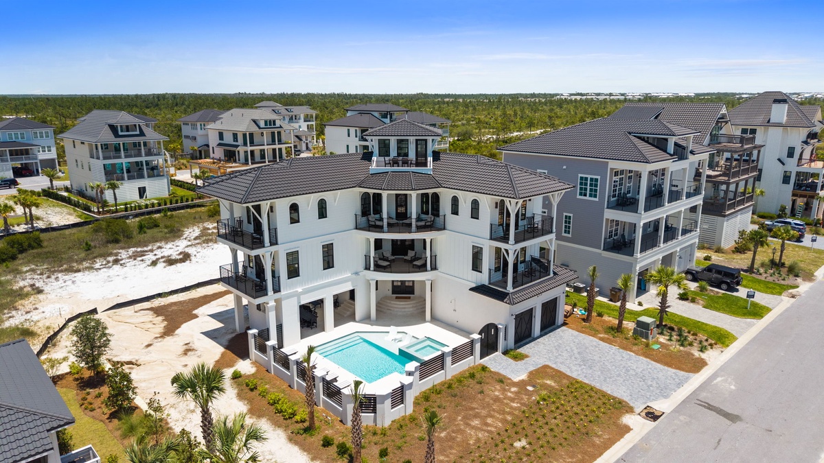 Coastal rental community showcasing the property's elegant exterior and private pool nestled among palm-lined grounds, just moments from sandy beaches and neighboring vacation homes.