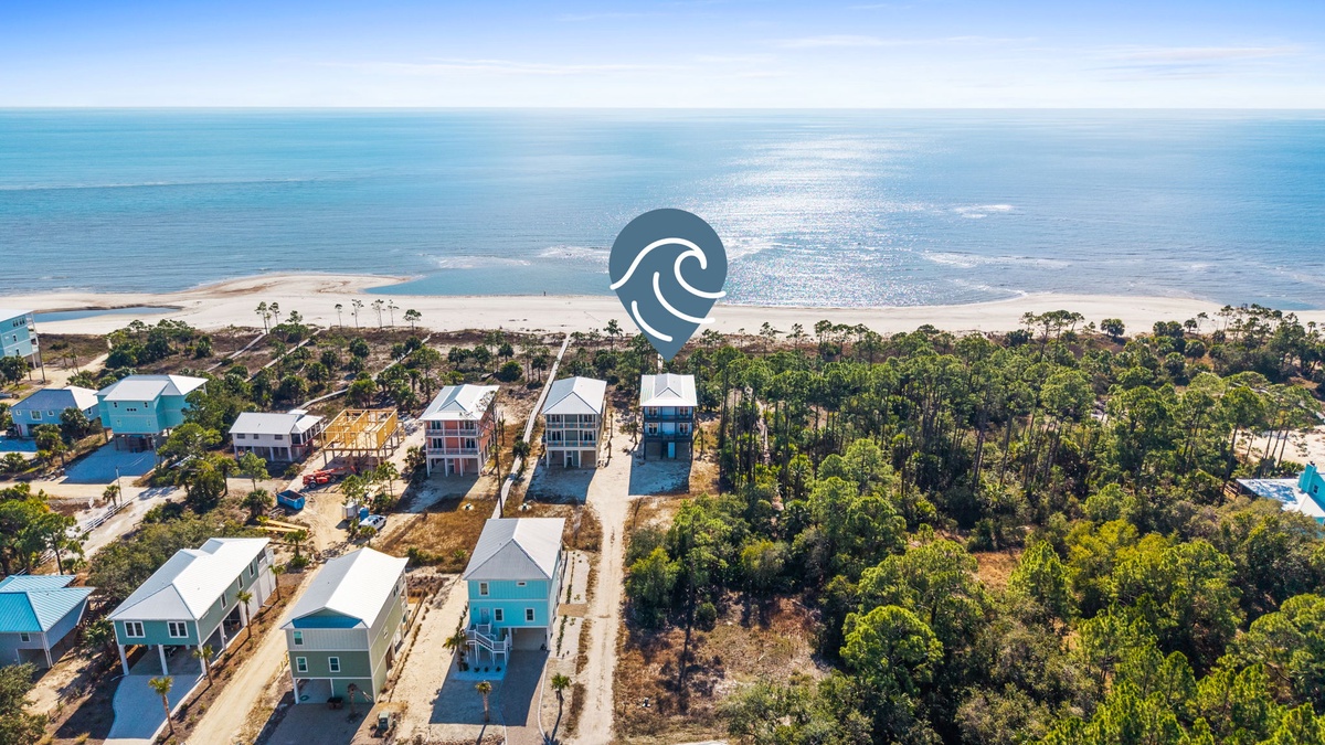 Coastal community with colorful beach houses nestled between lush forest and pristine sandy shores.