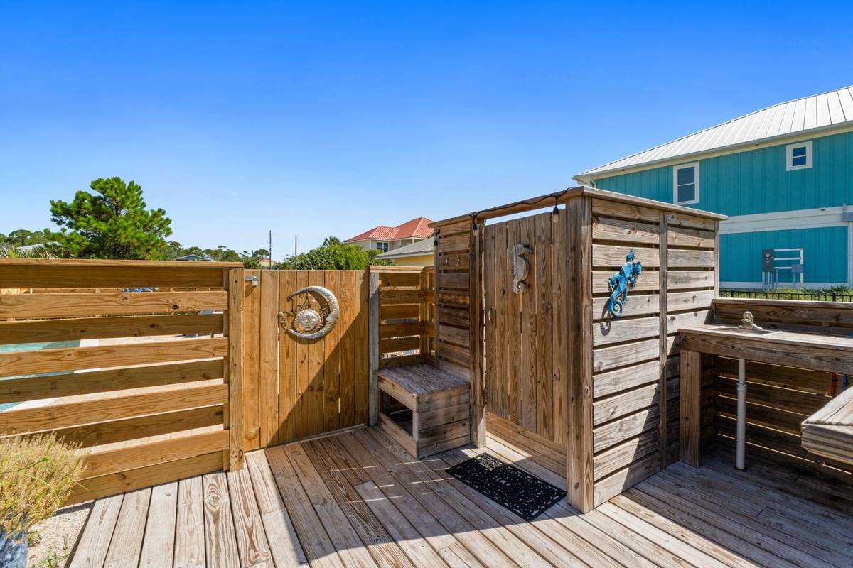 This charming coastal property features a distinctive turquoise exterior with white trim. Neighboring homes and natural landscaping create a relaxed beachside setting.