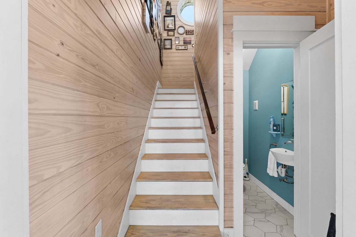 Warm wood paneling creates a cozy nautical feel as you climb the stairs, with a charming powder room tucked beneath.