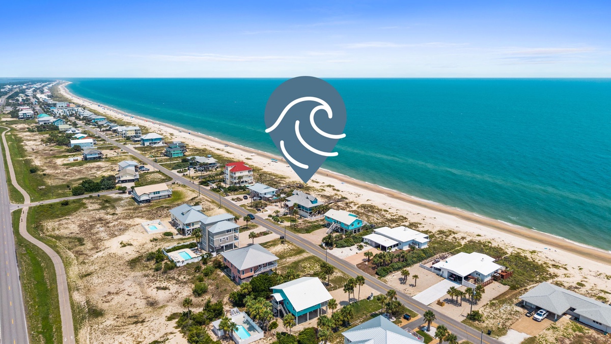 Aerial view of beachfront vacation homes nestled along pristine white sand and turquoise waters, offering a peaceful coastal community setting.