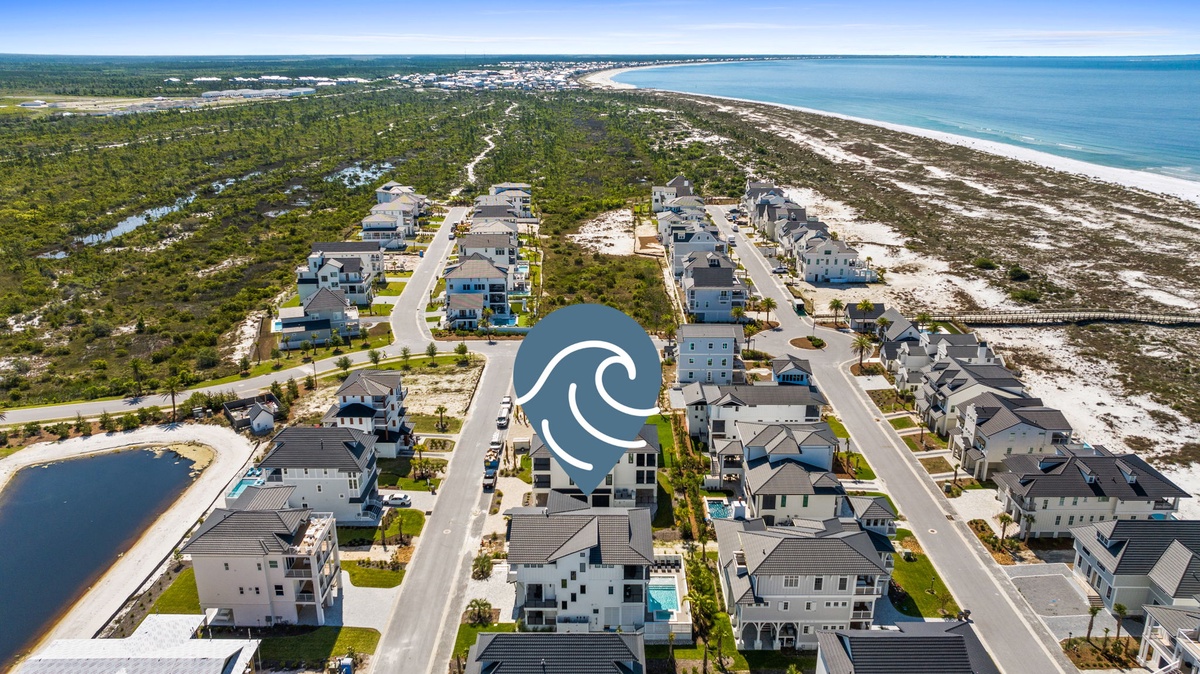 Aerial view showcasing the beachfront neighborhood, nestled between lush coastal vegetation and the sparkling turquoise Gulf waters, offering serene access to pristine sandy shores.