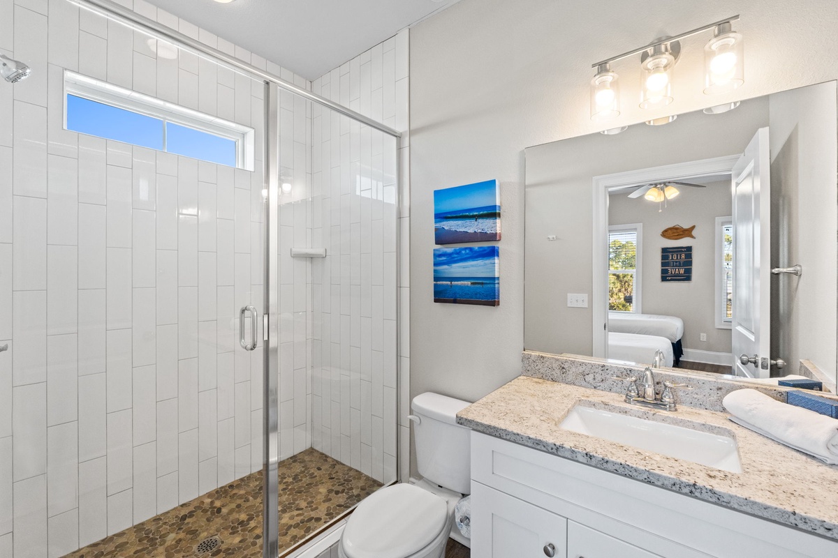 Your private bathroom features a spacious glass shower, elegant granite counters, and coastal artwork that brings seaside serenity to your daily routine.