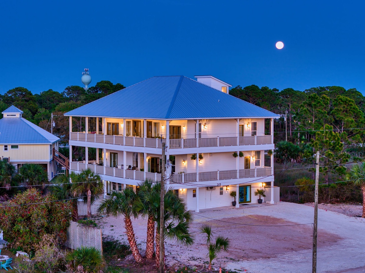 Stunning three-story coastal property with wraparound porches and tropical landscaping under moonlit skies near a historic water tower.