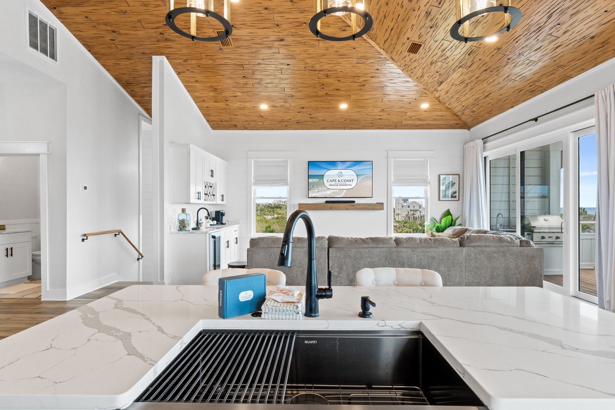 Gather around this sleek kitchen island where warm wood ceilings meet modern coastal style. Your gourmet space flows into the living area, perfect for entertaining with ocean views just beyond.
