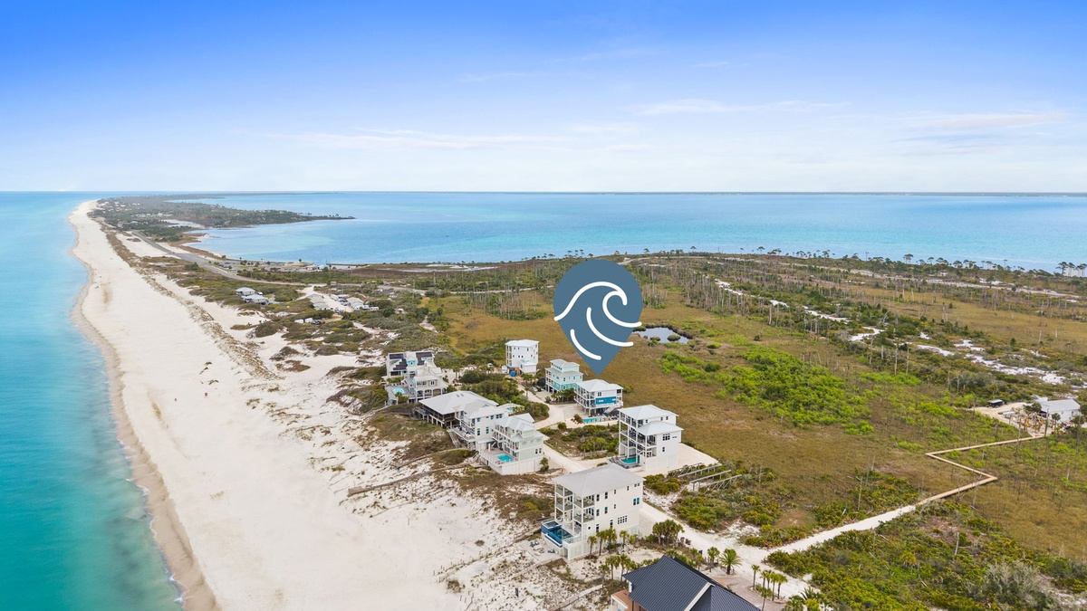 Pristine beachfront community with turquoise waters stretching to the horizon, featuring scattered coastal homes along miles of white sand.