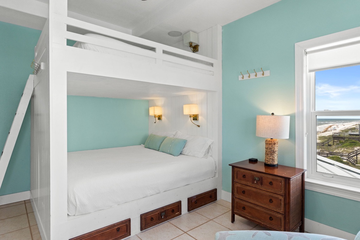 Your coastal retreat features a custom bunk bed with crisp white linens and built-in storage, perfect for families. Soft aqua walls and warm lighting create a serene, beachy vibe with stunning ocean views.