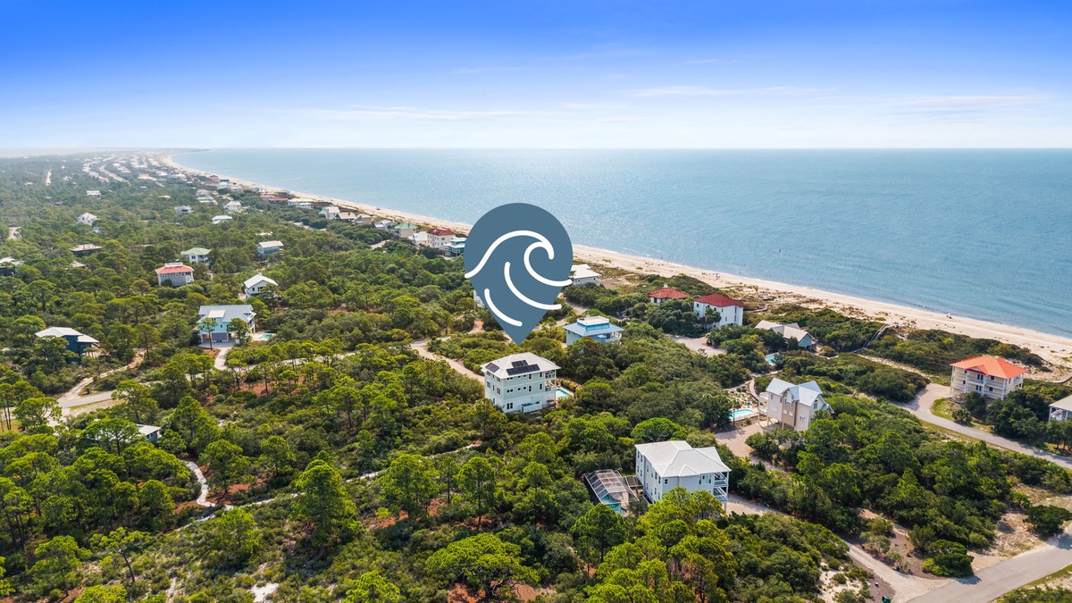 Aerial view of a peaceful beachfront community nestled among lush greenery, with sandy shores and calm turquoise waters stretching to the horizon.