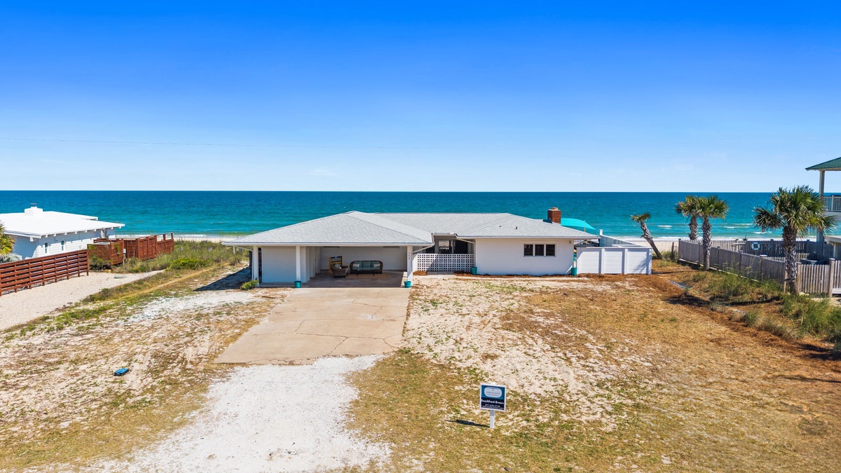Beachfront property offering direct access to pristine sandy shores and stunning turquoise waters, surrounded by coastal palms and neighboring beach homes.